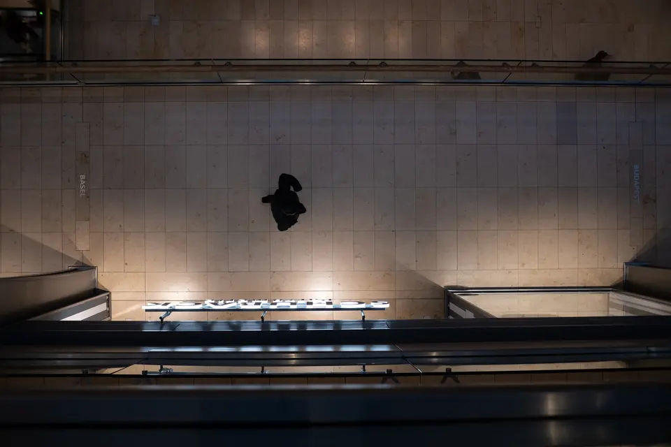 A dark object caught in mid-air above a lit shop sign and a tiled wall