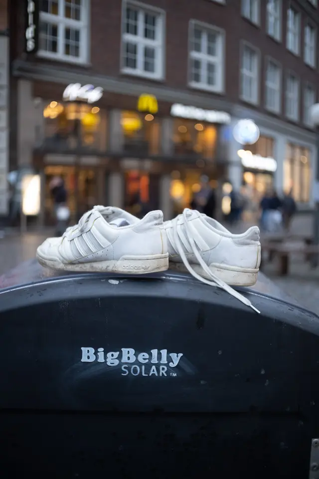 A pair of white trainers left on top of a street litter bin