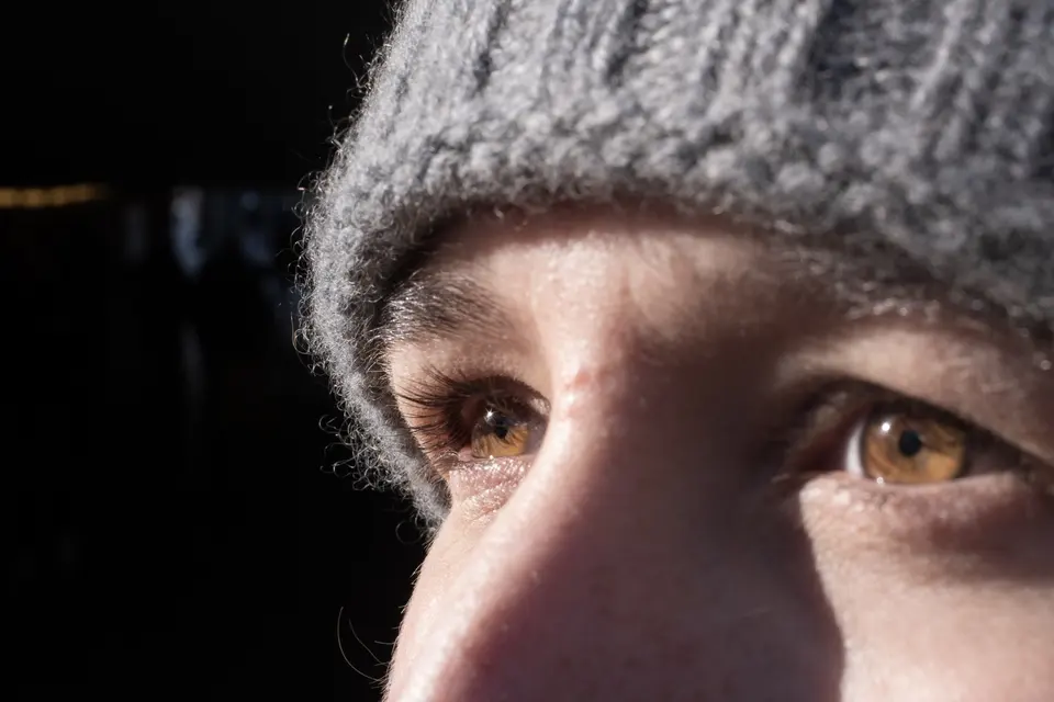 Close portrait: eyes and a grey knitted hat in warm side light