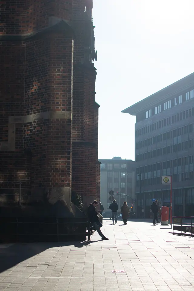 A brick church wall in shadow, small figures in the sunlit street beyond