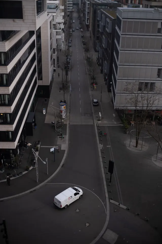 A white van on a curving street between office blocks, seen from above