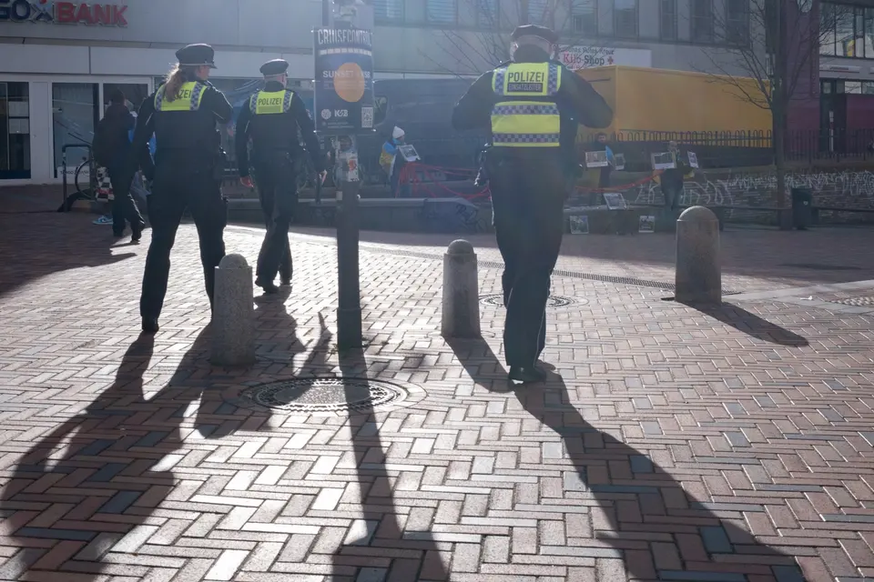 Three police officers walking away across a square, throwing long shadows