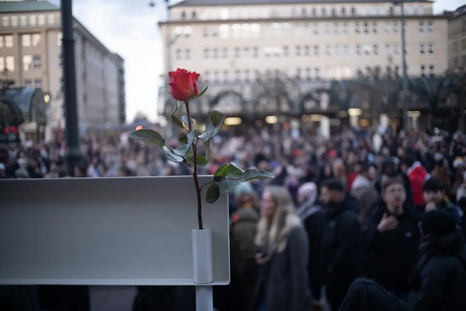 A single red rose fixed to a flag holder, the crowd out of focus behind it