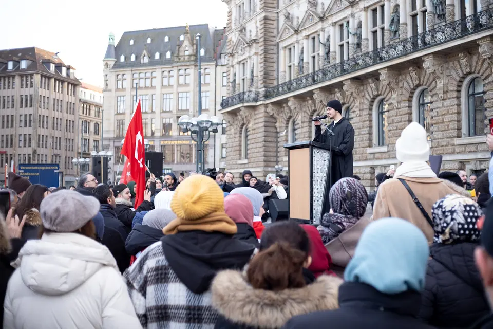 A speaker at a lectern in front of Hamburg town hall, seen over the heads of the crowd