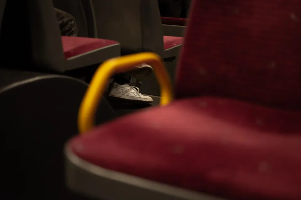 Red bus seats and a yellow handrail, a white trainer resting on the seat in front
