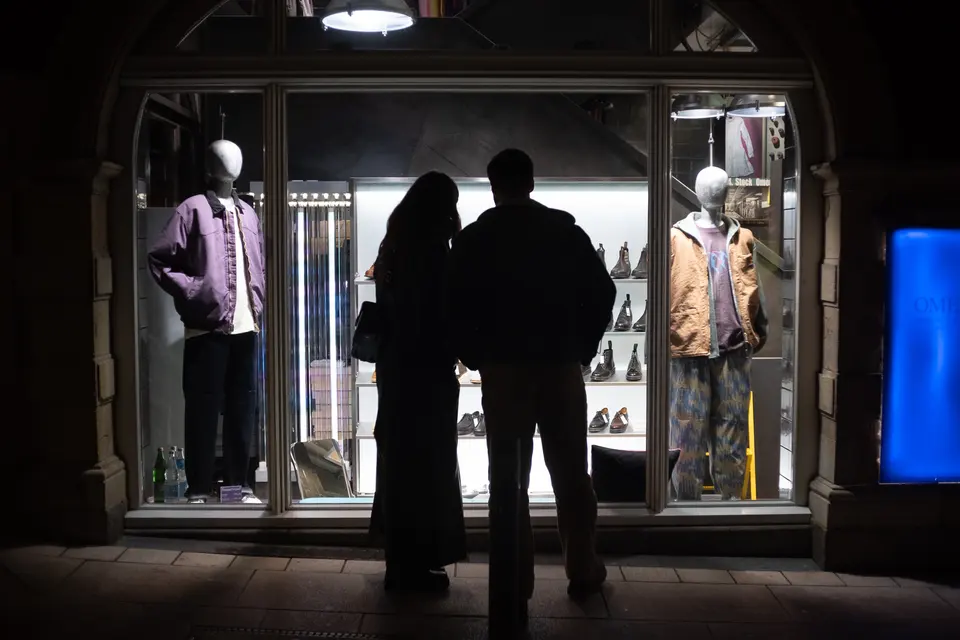 Two people in silhouette looking into a lit shop window at night