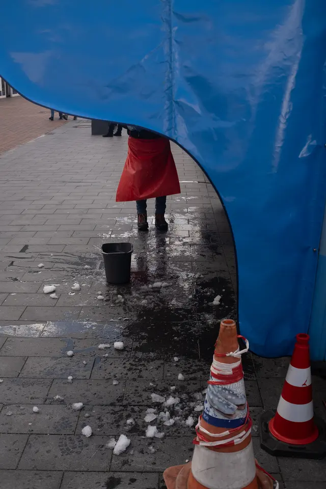 The corner of a blue market tarpaulin, a red skirt behind it and two traffic cones in front