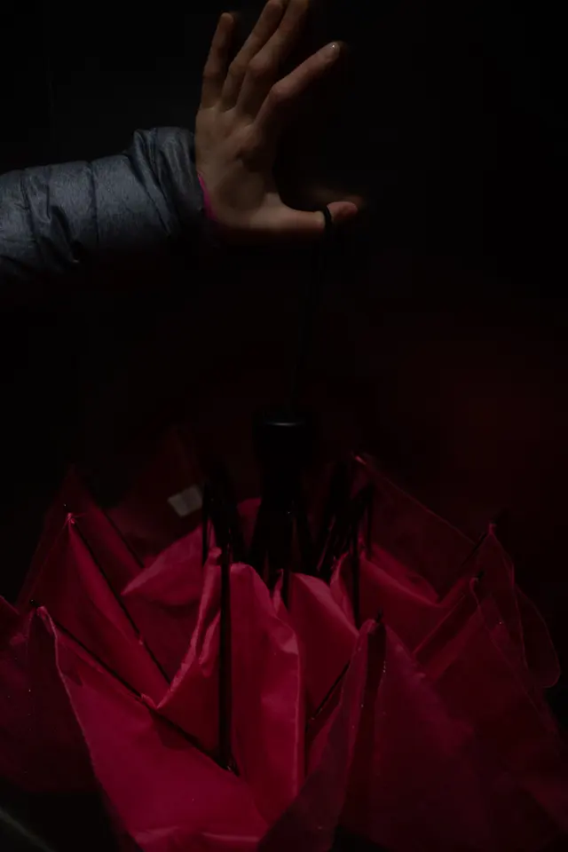 A raised hand above a folded red umbrella in the dark