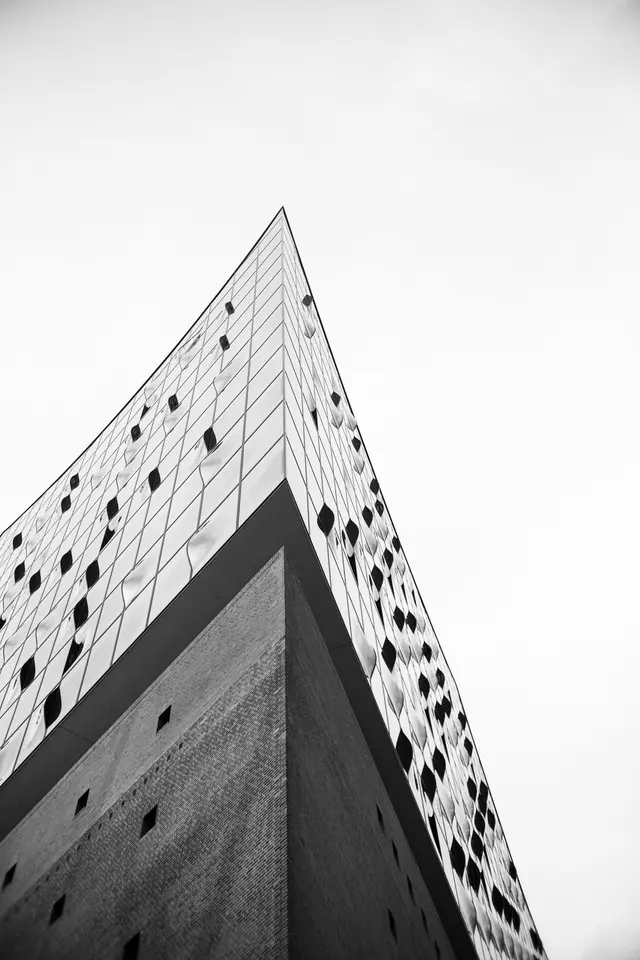 The corner of the Elbphilharmonie seen from below against a white sky, in black and white