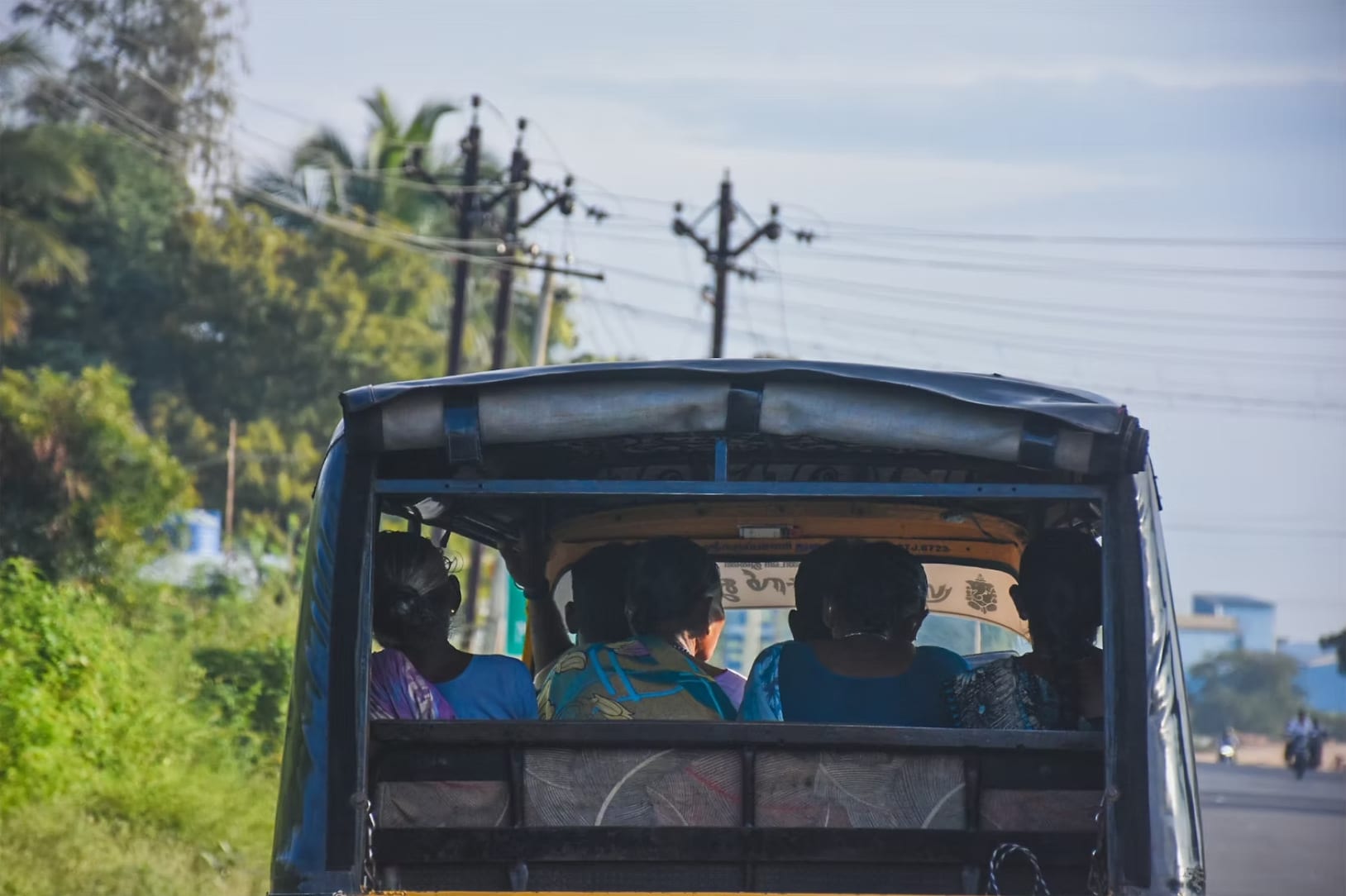 Passengers seen from behind in a shared vehicle on a road under power lines, South India, December 2020.