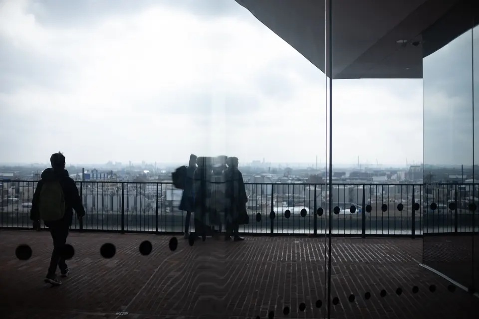 Visitors in silhouette on the Elbphilharmonie plaza, the city under cloud beyond the glass