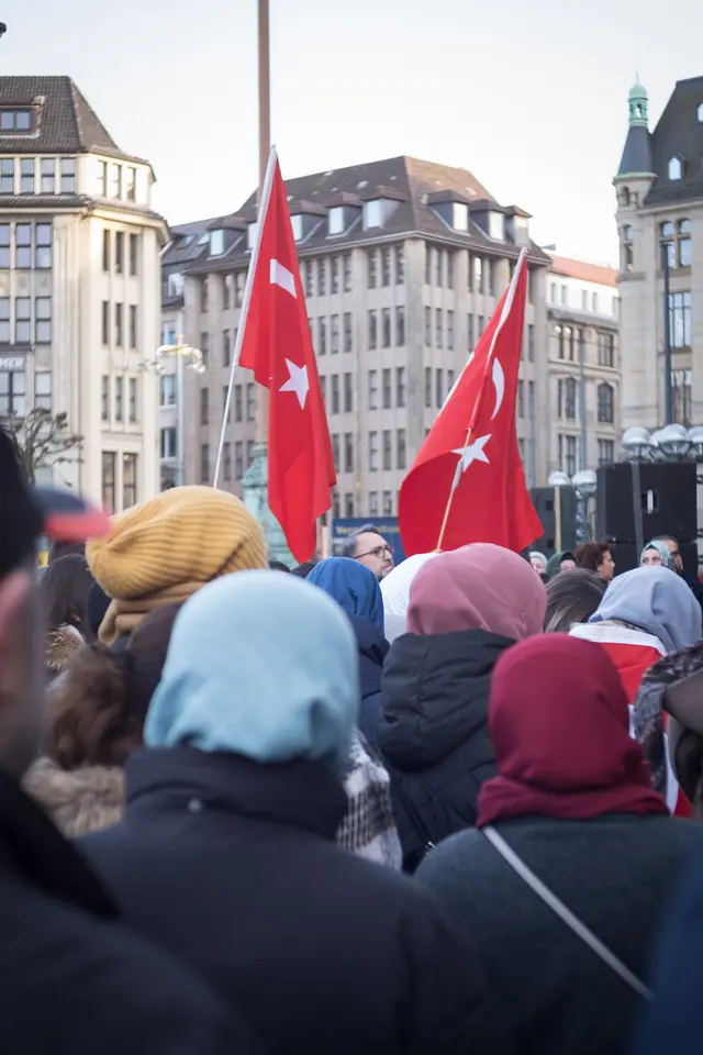 Crowd seen from behind on Hamburg's Rathausmarkt, two Turkish flags above the heads
