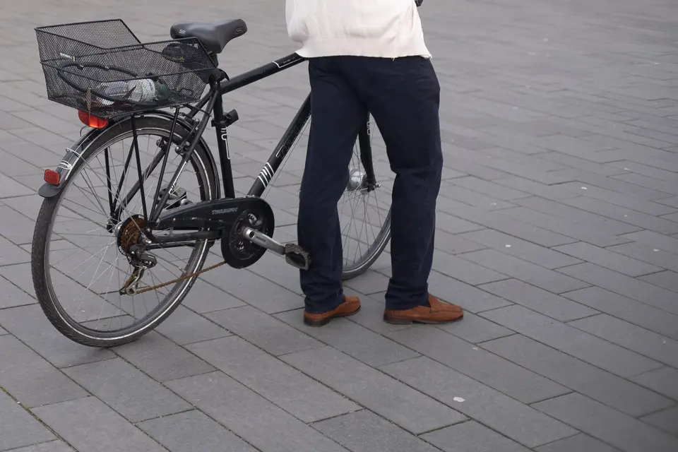 A person standing beside a black bicycle with a basket, cropped at the waist