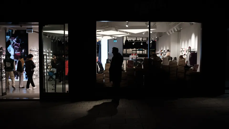 A lit shop interior seen from a dark street, a passer-by in silhouette