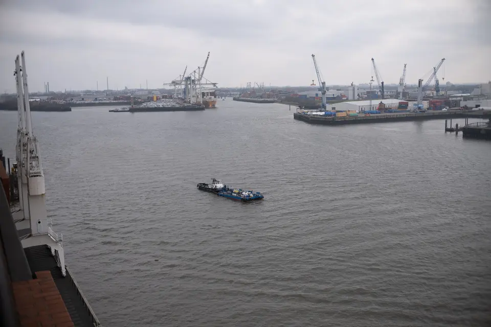 A barge crossing the Elbe, the container cranes of the port of Hamburg beyond