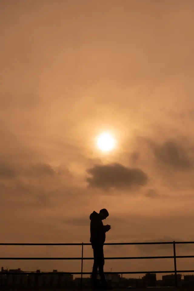A figure in silhouette at a railing under a hazy orange sun