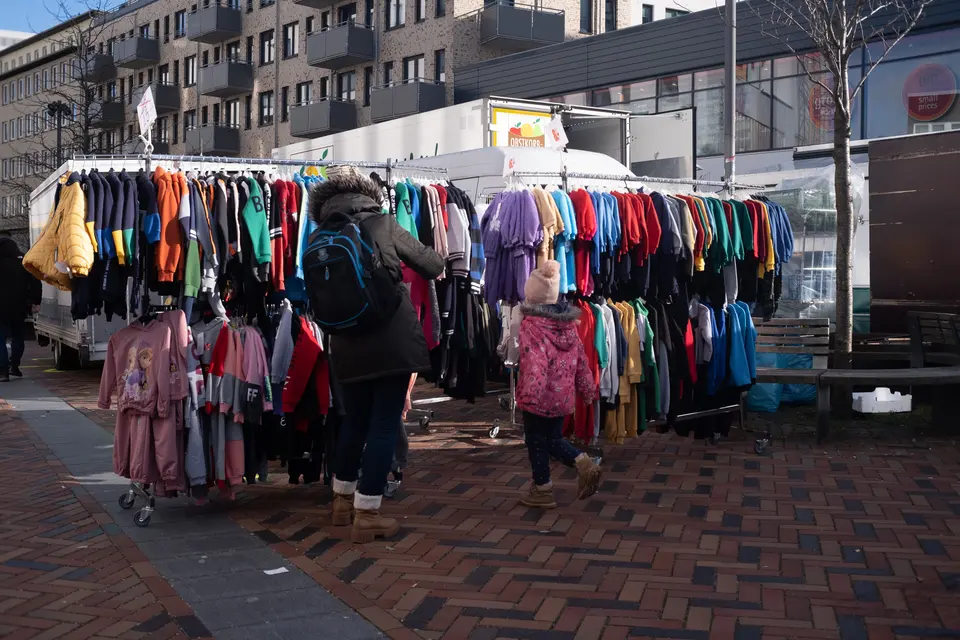 A market rail of colourful children's jackets, two shoppers seen from behind