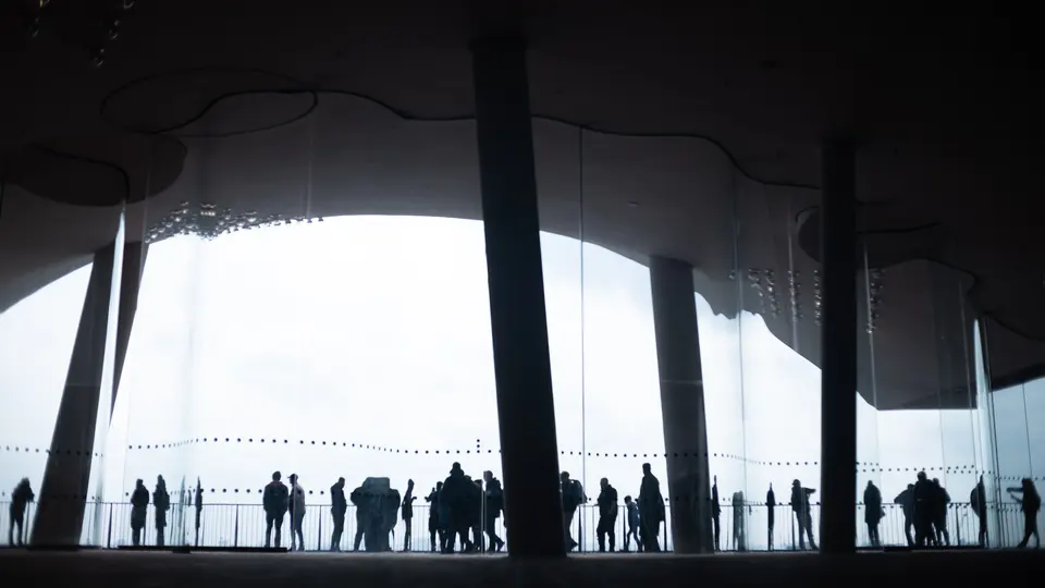 A row of visitors in silhouette under the curved roof of the Elbphilharmonie plaza