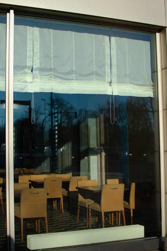 Empty chairs and tables behind a window that reflects trees and sky