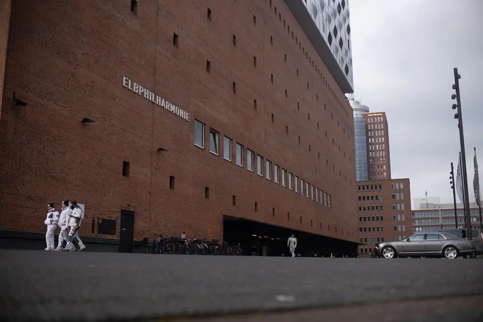 The brick base of the Elbphilharmonie, three people in white walking past